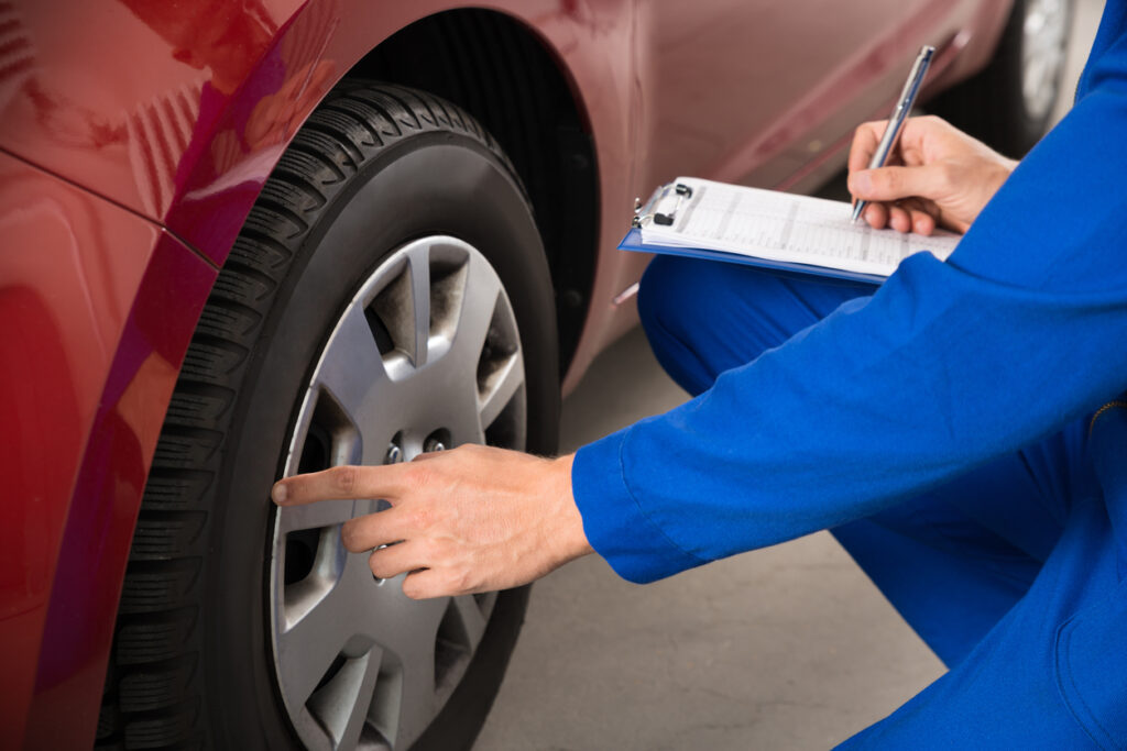 Young Mechanic Writing On Clipboard White Examining Car Wheel