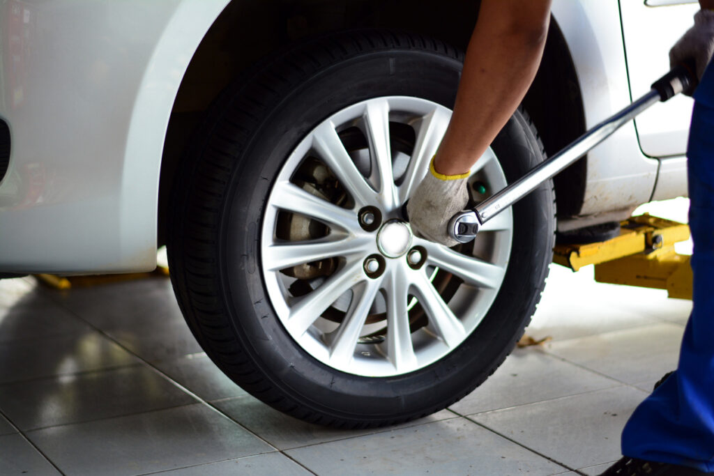 a mechanic in blue uniform with white glove holding a pound wrench tighten the bolts of the wheel