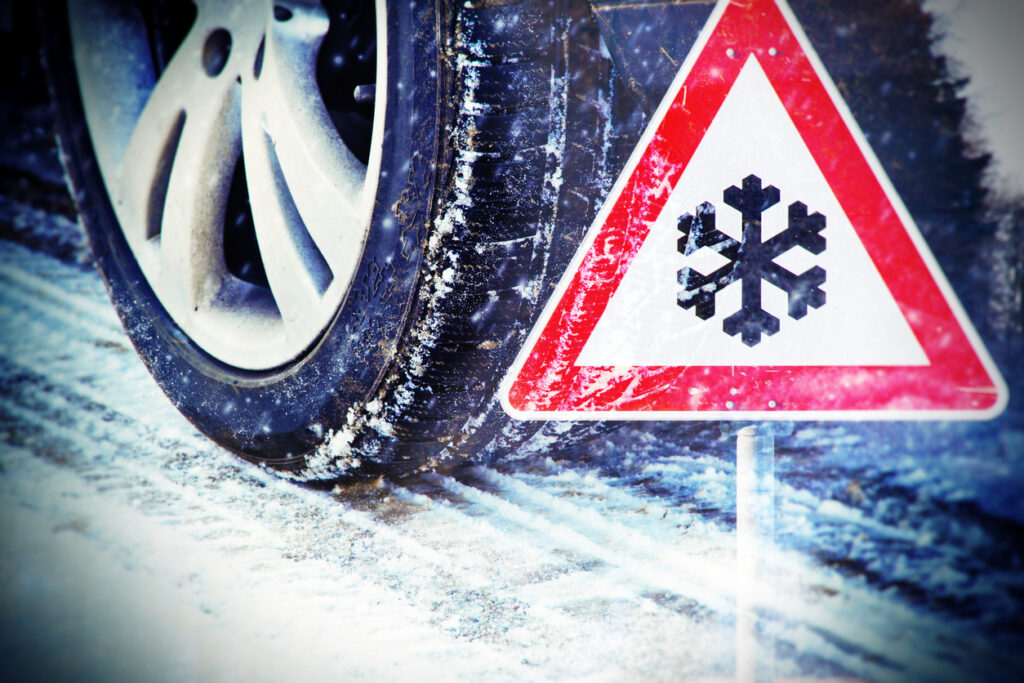 Car tires on winter road with traffic sign