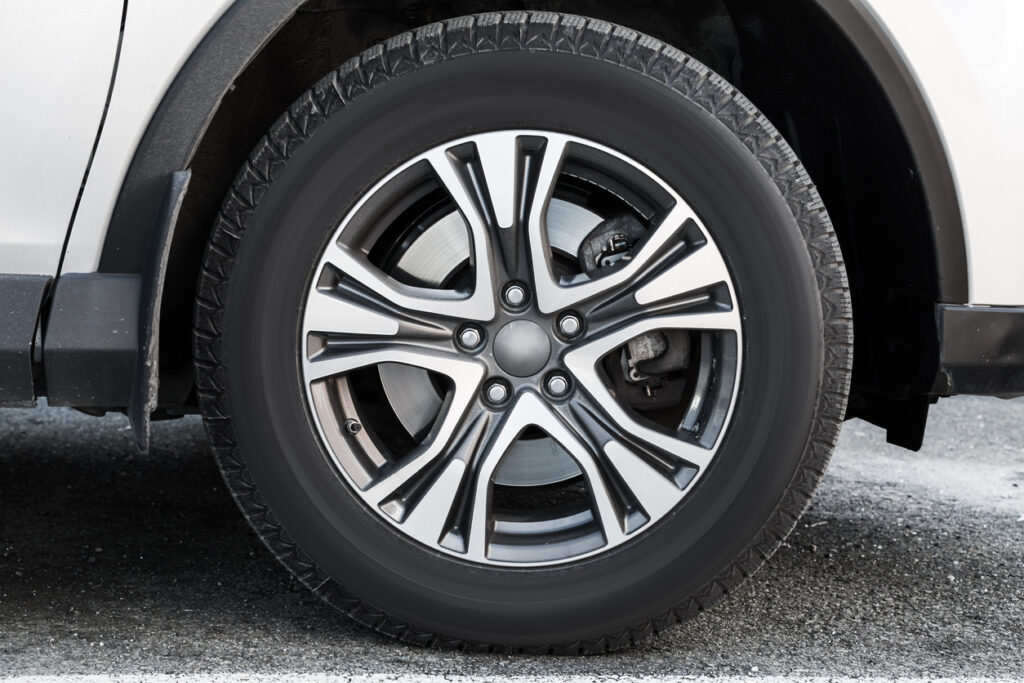 Fragment of white modern car with wheel on steel disc, closeup photo