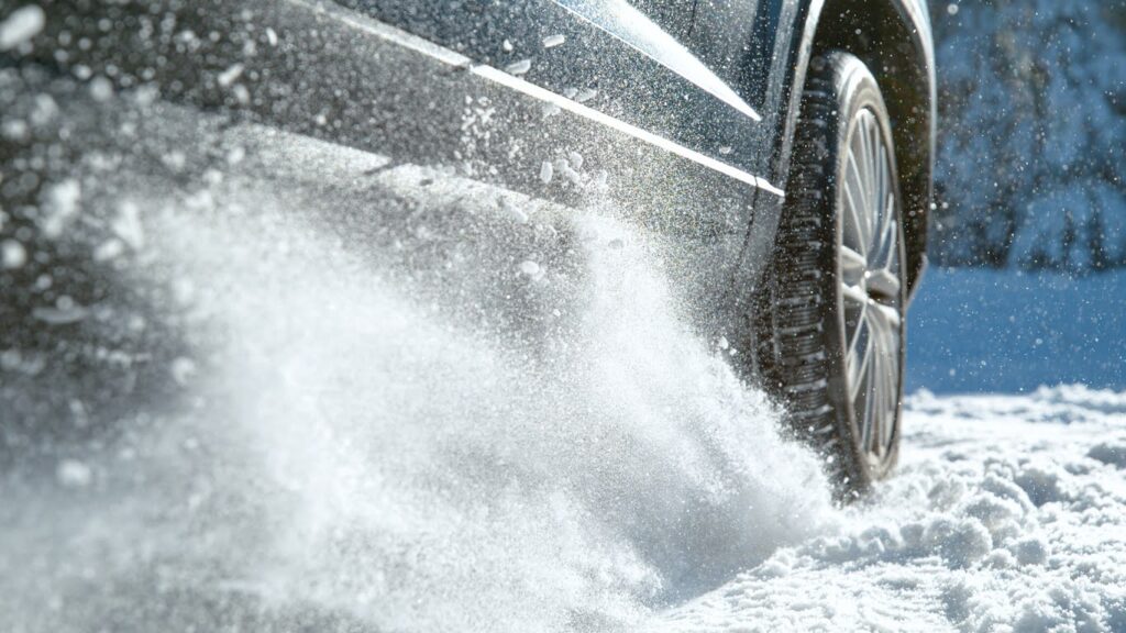 CLOSE UP: Cinematic low angle shot of vehicle having problems driving along the snow covered trail. Glistening small chunks of fresh snow fly in the air as powerful car tries to start on a snowy road.