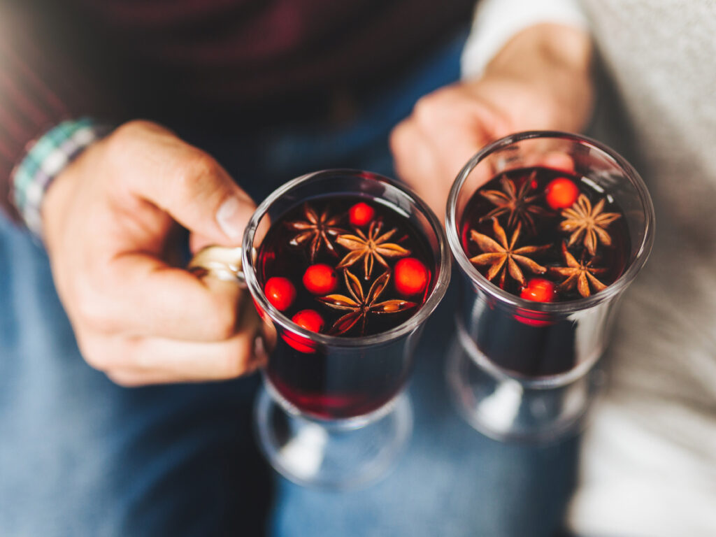 Crop people clinking with glasses full of mulled wine withs spices.