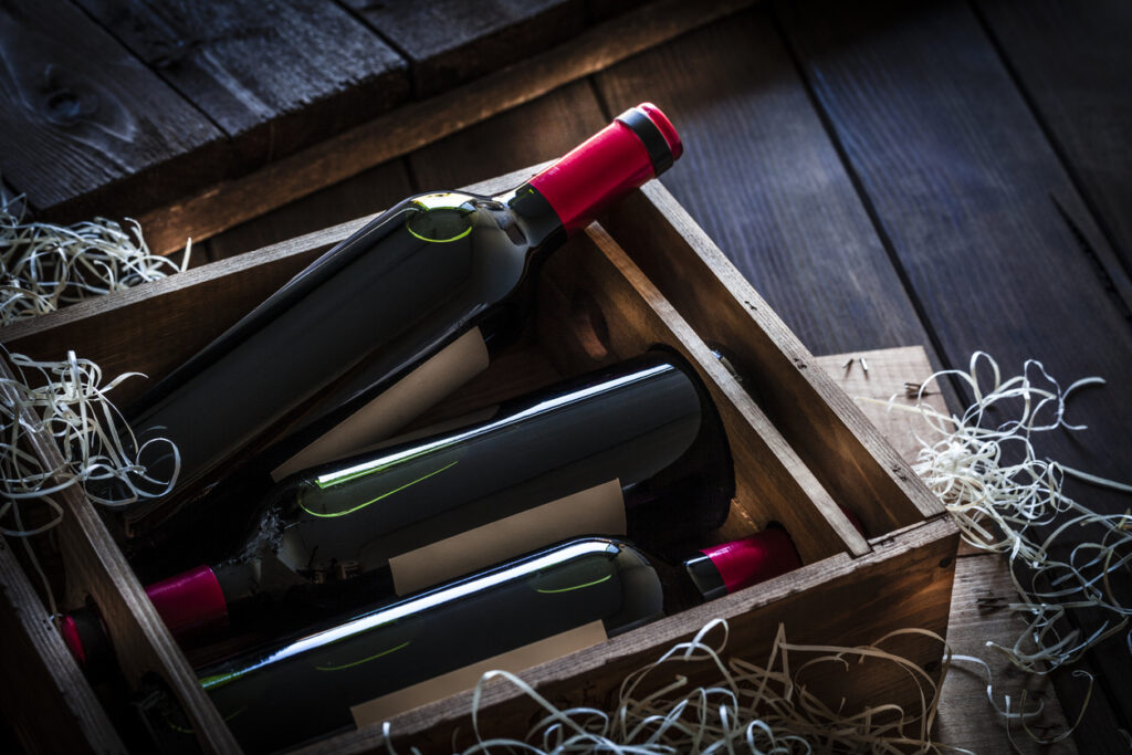 High angle view of a wooden box with three red wine bottles shot on rustic wooden table. The labels on the bottles are blank so you can put any design on them. Predominant color is brown.