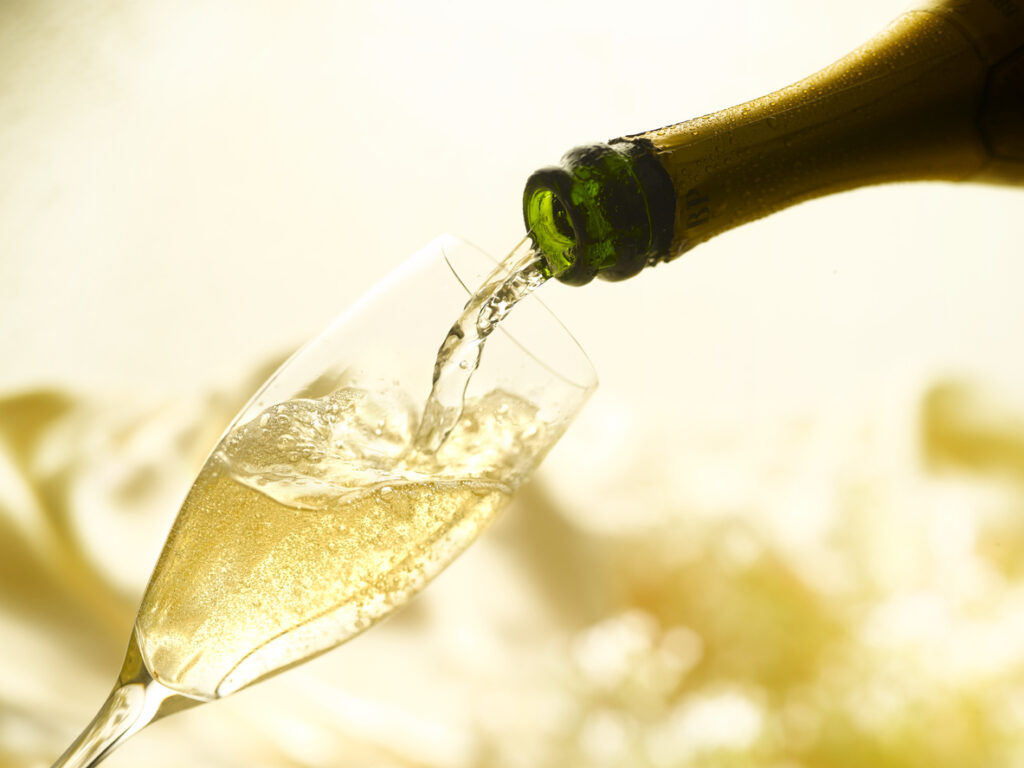Champagne being poured from a bottle into a classic champagne flute glass.