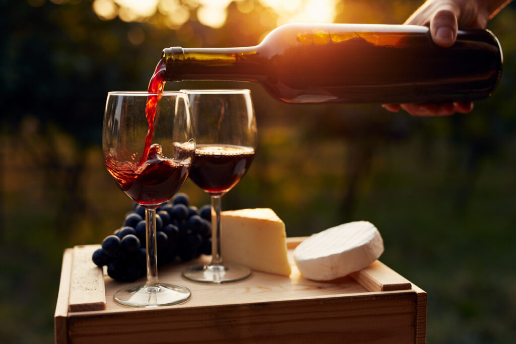 Pouring red wine into the glass in the vineyard at sunset