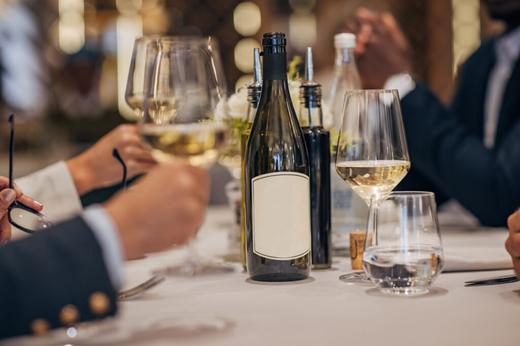 Diverse people, white wine on table in front of unrecognizable people in luxury restaurant.