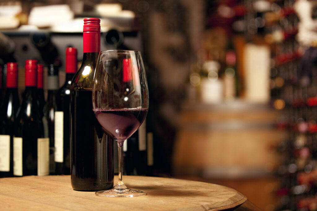 Tasting red wine in a privately owned cellar underground. There is a bottle of red wine, a glass of red wine and a barrel can be seen in the background.
