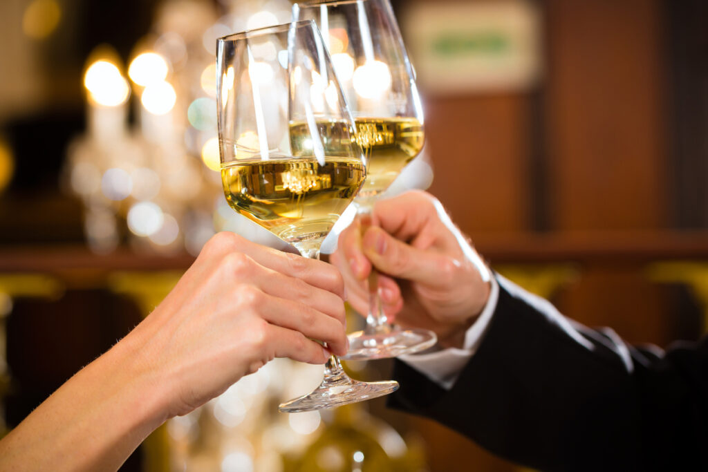 happy couple have a romantic date in a fine dining restaurant they drink wine and clinking glasses, cheers - a large chandelier is in Background