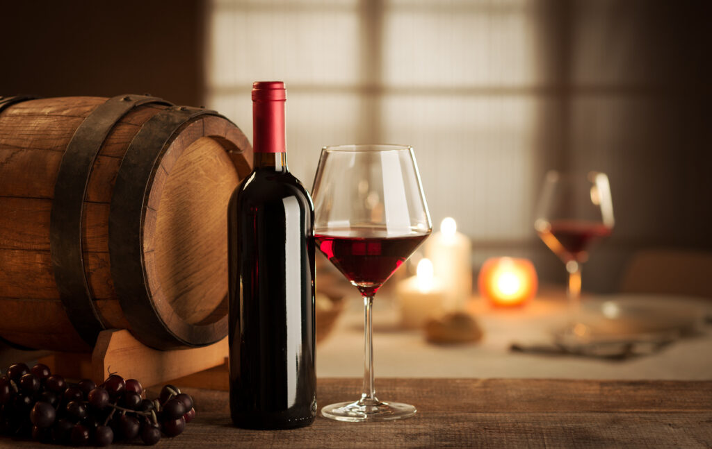 Bottle, glass, grape and barrel still life with restaurant on background.
